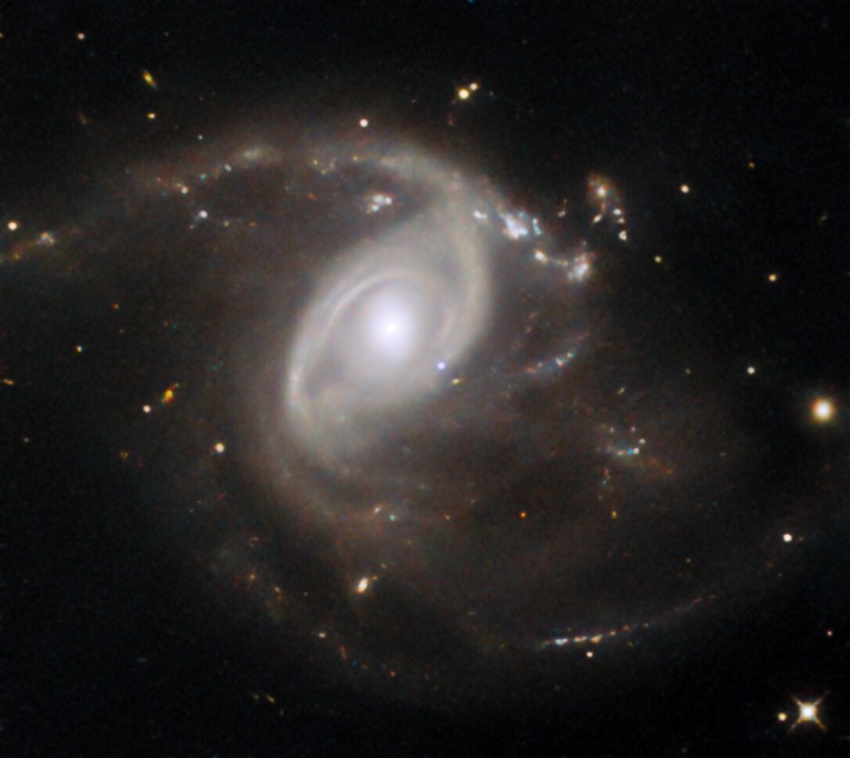 This NASA/ESA Hubble Space Telescope Picture of the Week features the galaxy LEDA 22057, which is located about 650 million light-years away in the constellation Gemini. Like the subject of last week’s Picture of the Week, LEDA 22057 is the site of a supernova explosion. This particular supernova, named SN 2024PI, was discovered by an automated survey in January 2024. The survey covers the entire northern half of the night sky every two days and has catalogued more than 10 000 supernovae. The supernova is visible in this image: located just down and to the right of the galactic nucleus, the pale blue dot of SN 2024PI stands out against the galaxy’s ghostly spiral arms. This image was taken about a month and a half after the supernova was discovered, so the supernova is seen here many times fainter than its maximum brilliance. SN 2024PI is classified as a Type Ia supernova. This type of supernova requires a remarkable object called a white dwarf, the crystallised core of a star with a mass less than about eight times the mass of the Sun. When a star of this size uses up the supply of hydrogen in its core, it balloons into a red giant, becoming cool, puffy and luminous. Over time, pulsations and stellar winds cause the star to shed its outer layers, leaving behind a white dwarf and a colourful planetary nebula. White dwarfs can have surface temperatures higher than 100 000 degrees and are extremely dense, packing roughly the mass of the Sun into a sphere the size of Earth.  While nearly all of the stars in the Milky Way will one day evolve into white dwarfs — this is the fate that awaits the Sun some five billion years in the future — not all of them will explode as Type Ia supernovae. For that to happen, the white dwarf must be a member of a binary star system. When a white dwarf syphons material from a stellar partner, the white dwarf can become too massive to support itself. The resulting burst of runaway nuclear fusion destroys the white dwarf in a supern