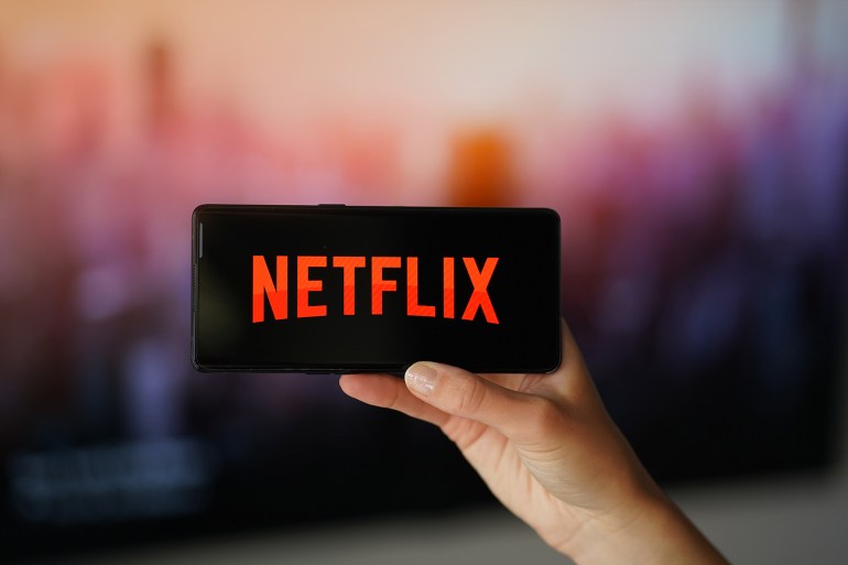 Rzeszow, Poland - 18 May 2024: netflix raises prices for subscribers. Woman holding the cell phone in hand with Netflix Logo. Warm tones, orange ; Shutterstock ID 2466539599; purchase_order: aj; job: ; client: ; other: