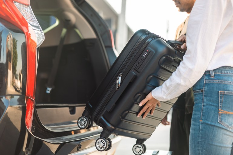 Happy couple puts his suitcase in the back of the car and prepares to leave for honeymoon trip. Husband and wife open the back of the car put luggage travel. Couple moving into new home at moving day