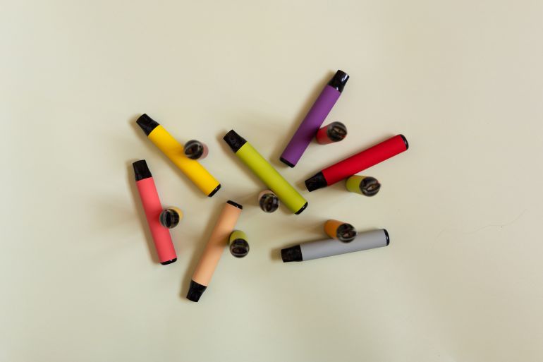 Assortment of colorful disposable vapor sticks, e-cigarettes on light background